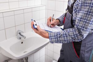 Plumber Standing In Front Of Washbasin Writing On Clipboard